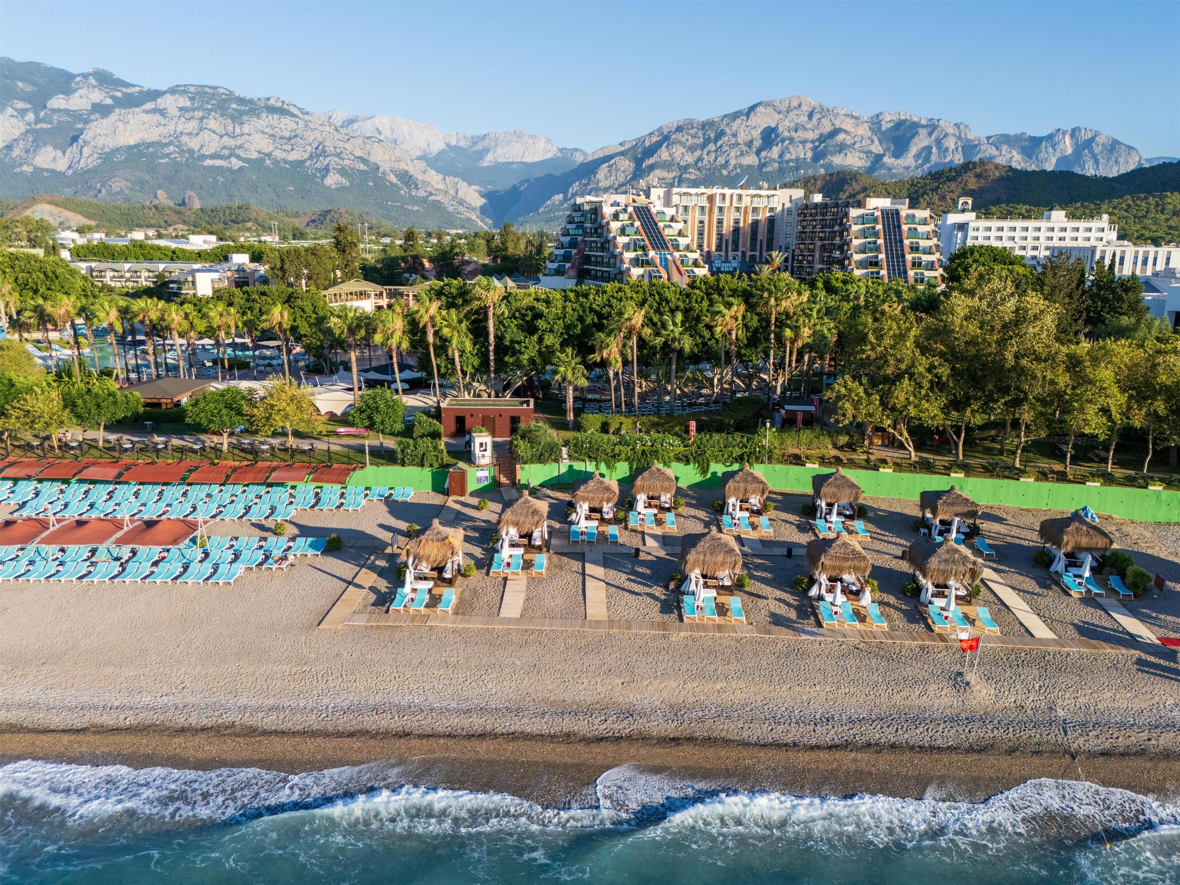 A beach resort with thatched umbrellas, sun loungers, and a view of mountains.