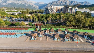 A beach resort with thatched umbrellas, sun loungers, and a view of mountains.