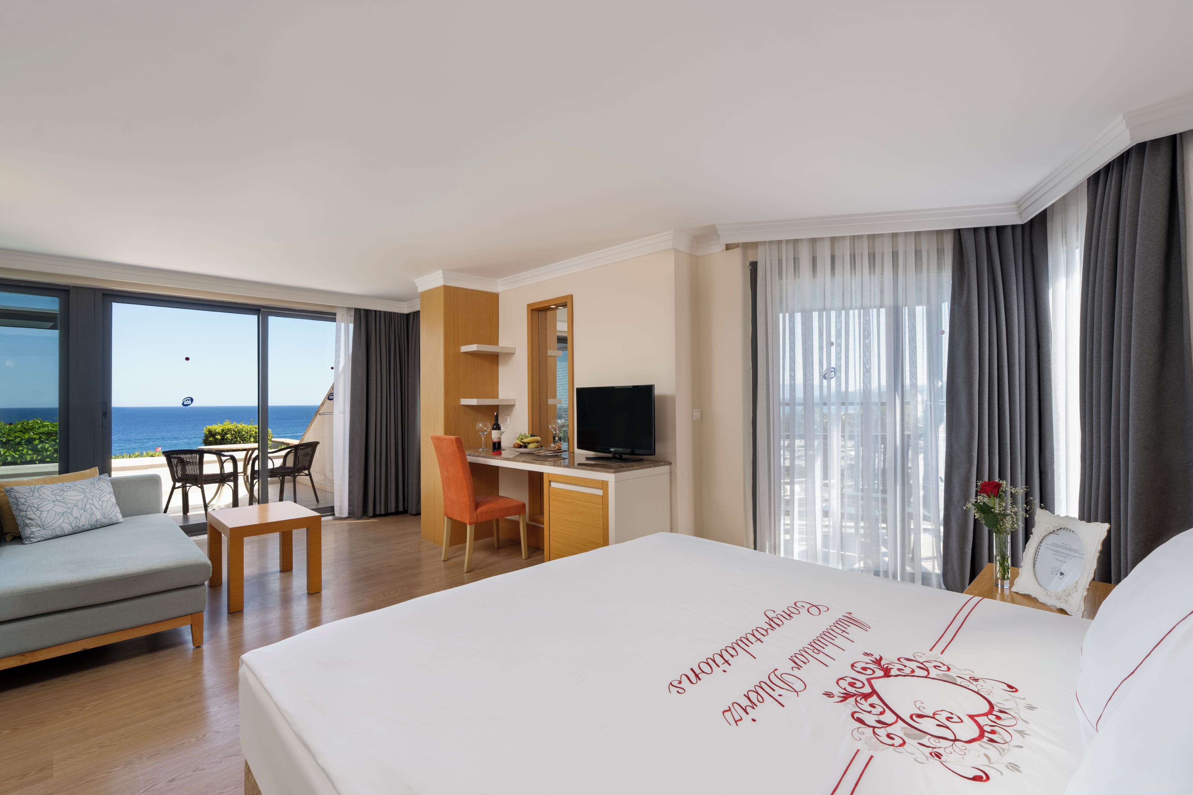 Habitación de hotel con cama, escritorio, silla, sofá, televisor y vista al océano.