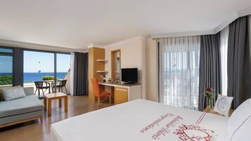 Habitación de hotel con cama, escritorio, silla, sofá, televisor y vista al océano.