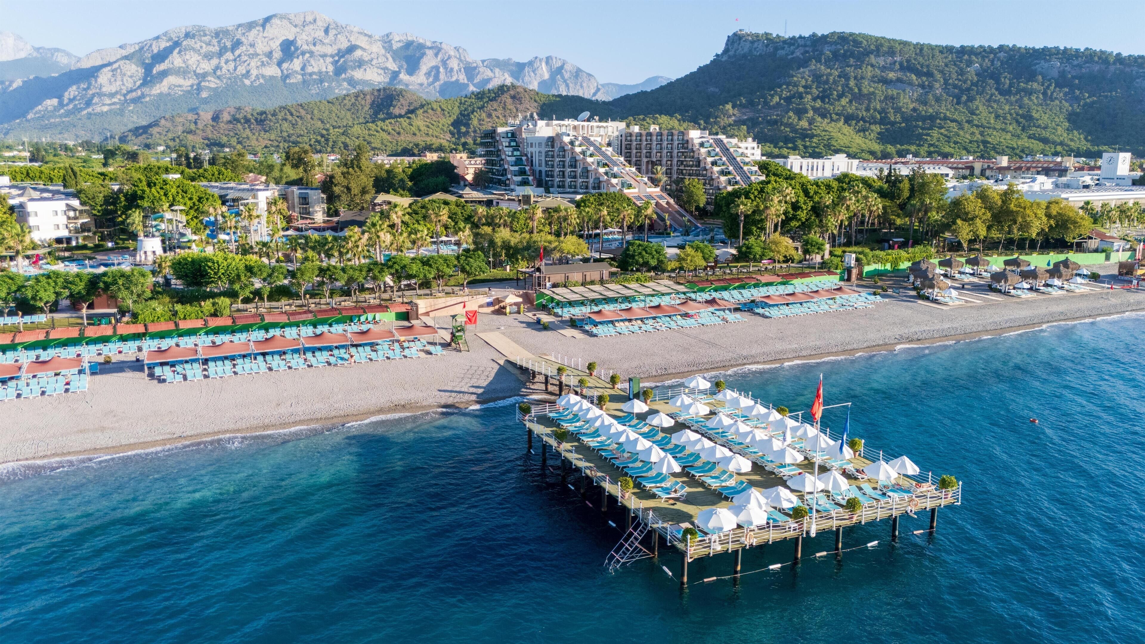 Un hotel frente al mar con un muelle que se adentra en el océano, que ofrece tumbonas y sombrillas.