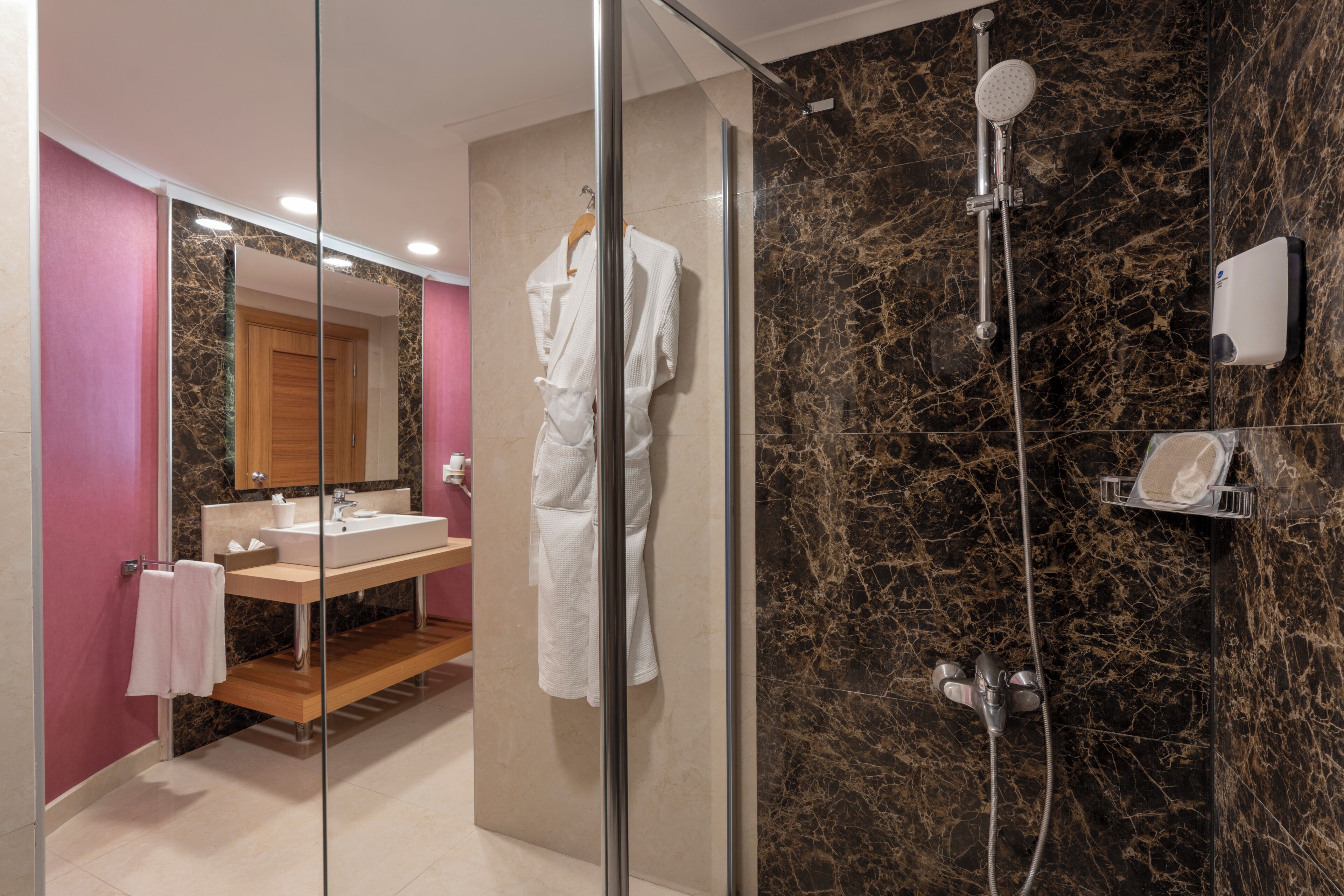 A modern bathroom with a glass shower enclosure, a vanity with a mirror, and a marble wall.