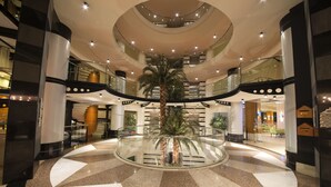 A multi-level atrium with a central glass railing, palm trees, and a polished floor. - Limak Limra Hotel & Resort  (Kemer)