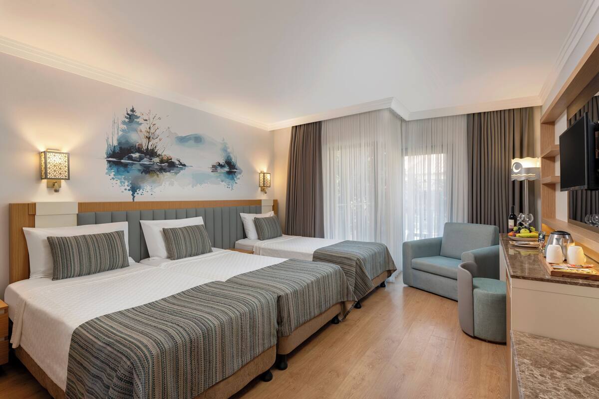 A hotel room with two beds, a sofa, a TV, and a painting on the wall.