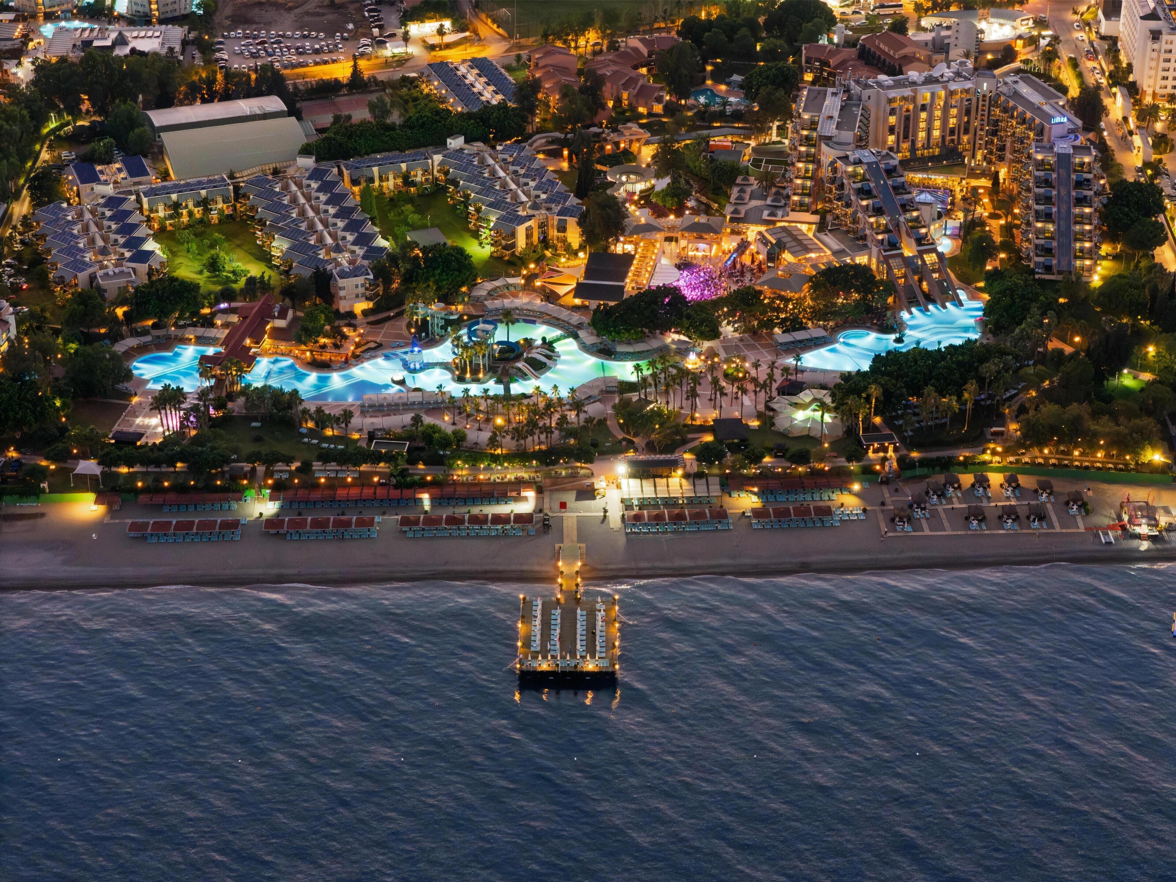 An aerial view of a resort with multiple buildings, a swimming pool, and a pier extending into the water.