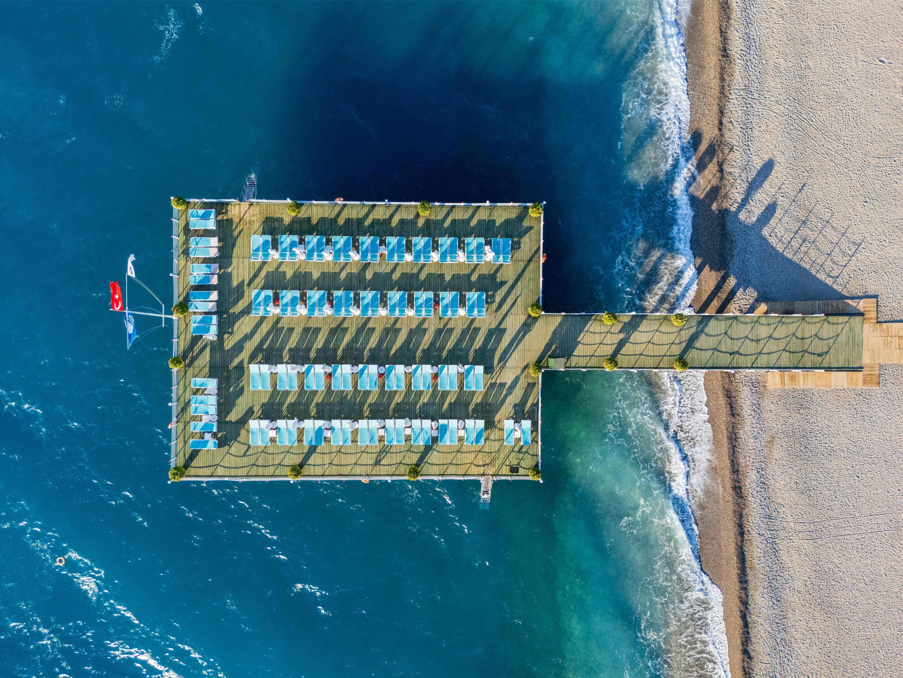 An aerial view of a coastal hotel with multiple rows of sun loungers and a flag.