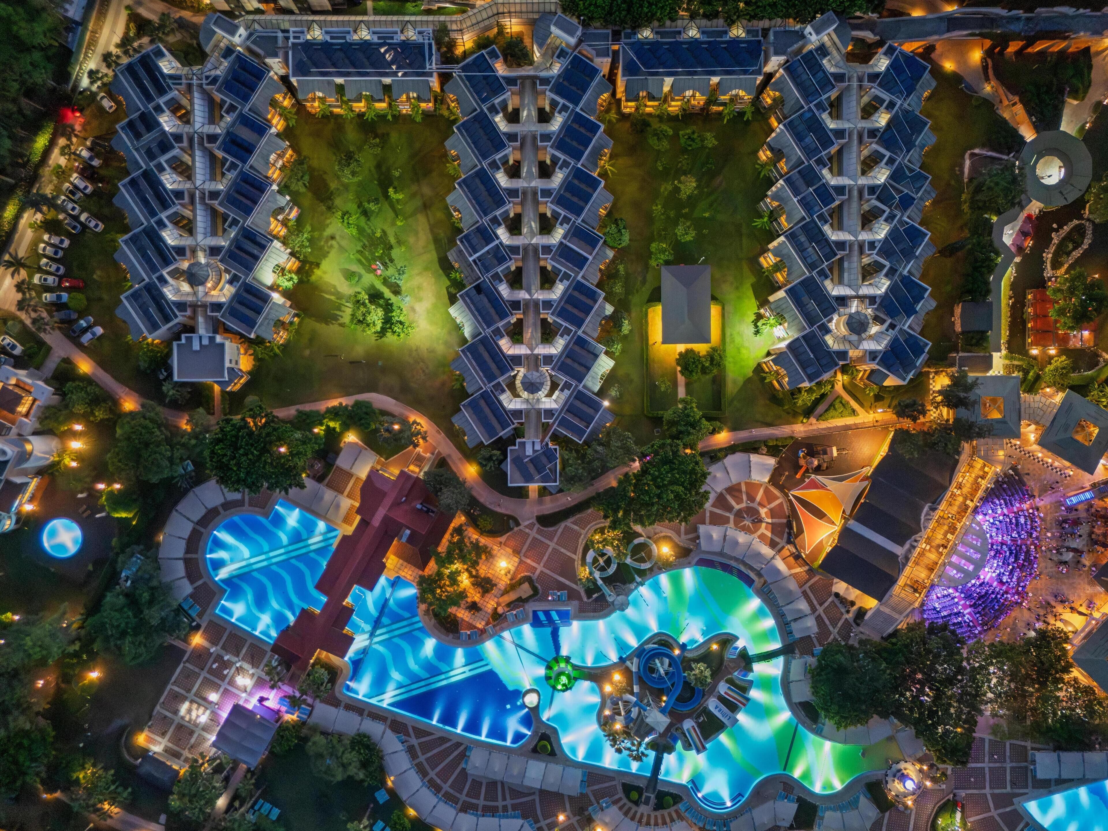 Vista aérea de un hotel con varias edificaciones, un área de piscina central y follaje circundante.