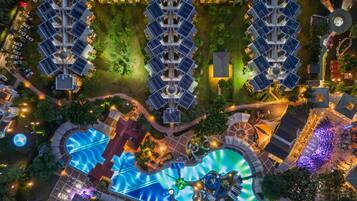 Vista aérea de un hotel con varias edificaciones, un área de piscina central y follaje circundante.