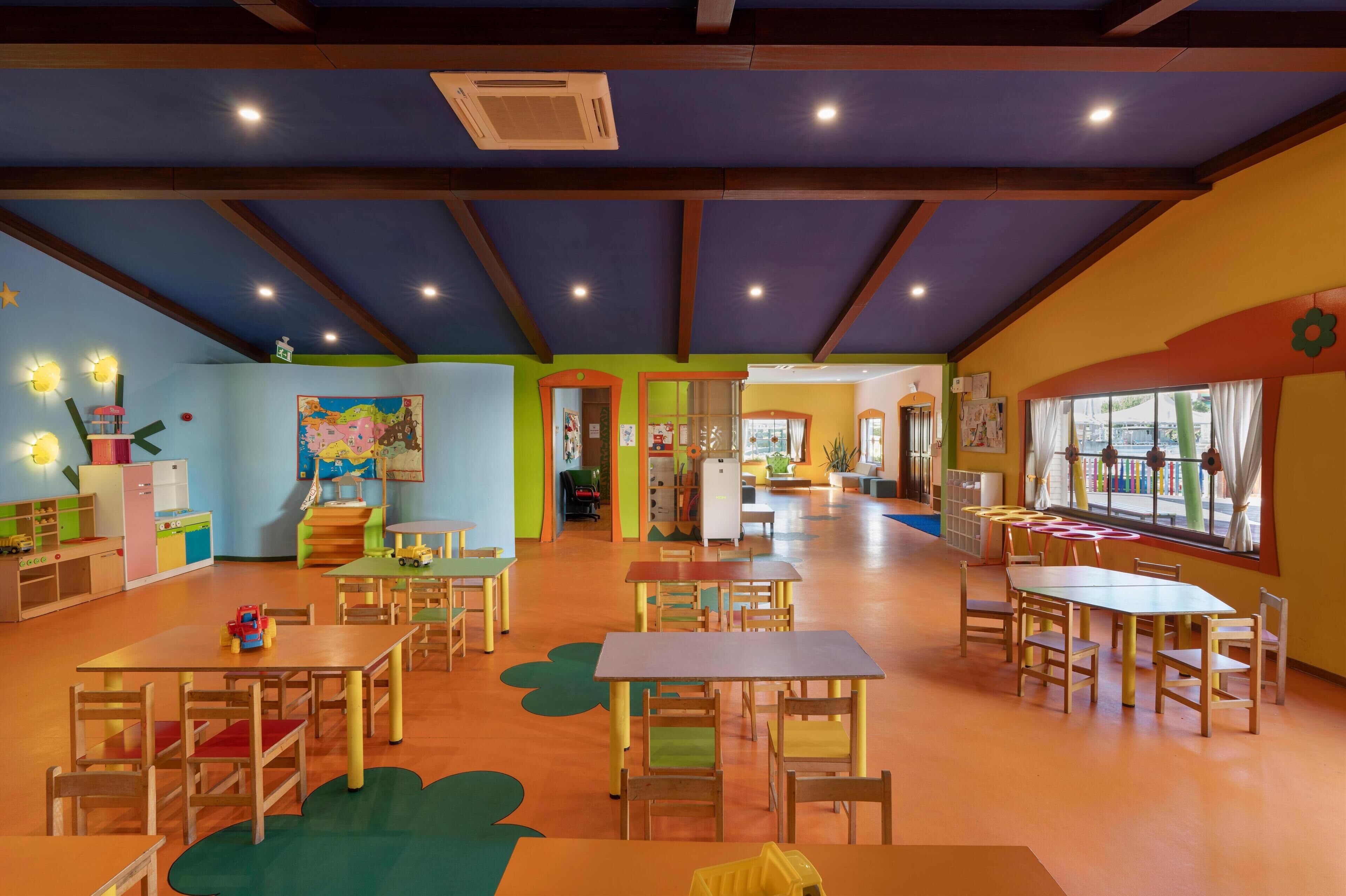 Una sala giochi per bambini con tavoli e sedie, giocattoli educativi e pareti colorate.
