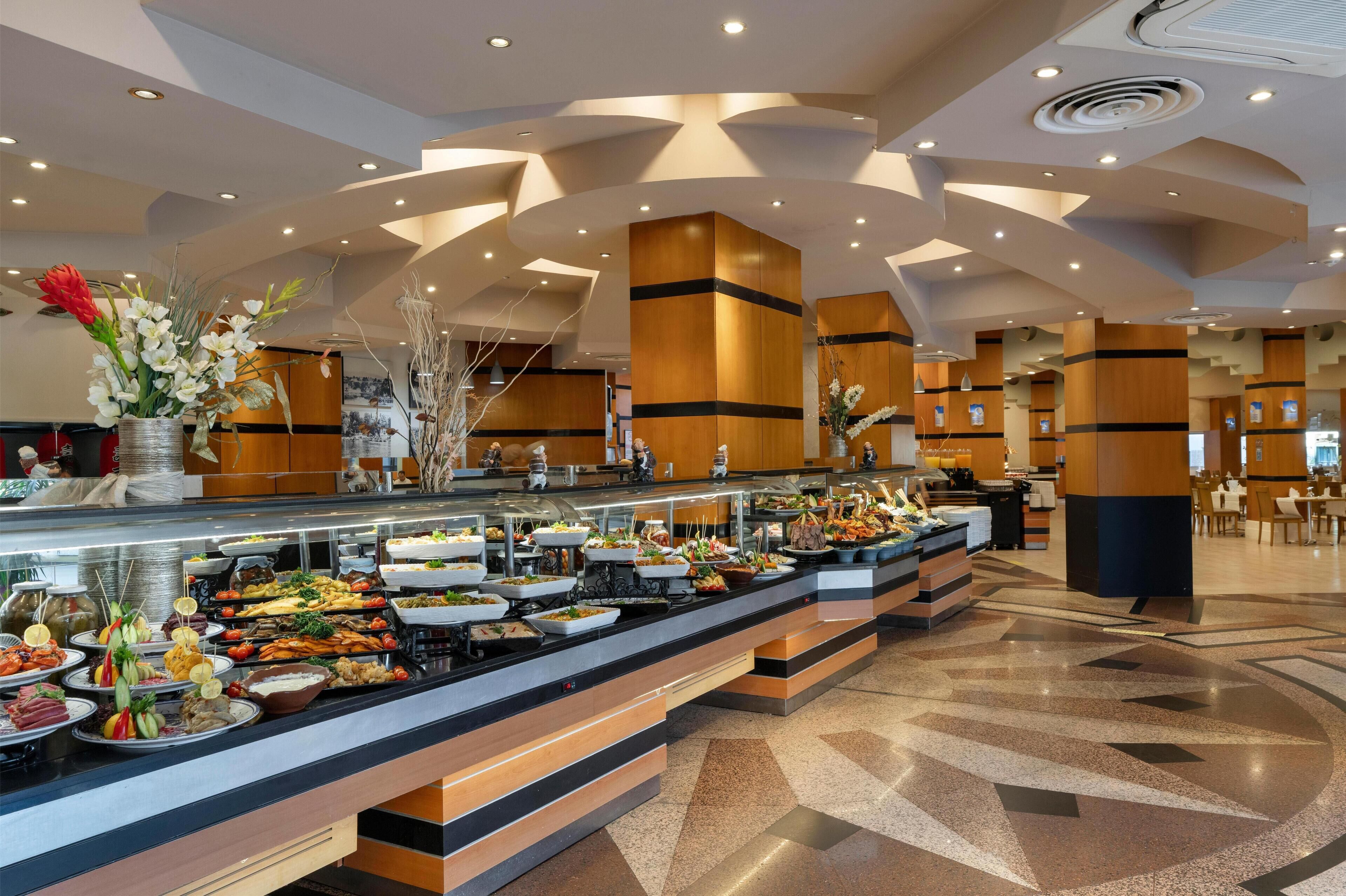 Zona de bufé con diversas opciones de comida, un diseño de techo moderno y un ambiente limpio y bien iluminado.