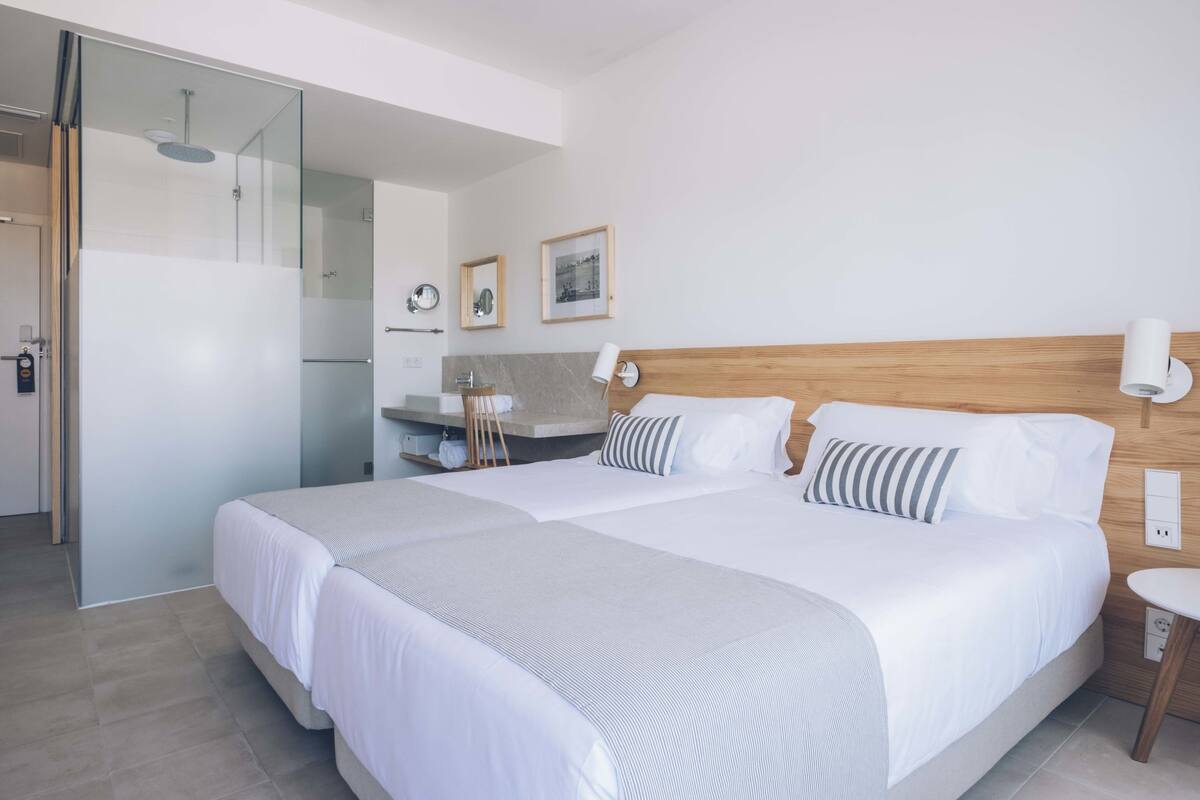 Ein modernes Hotelzimmer mit einem großen Bett, einem Nachttisch, einem Spiegel und einer Duschkabine.