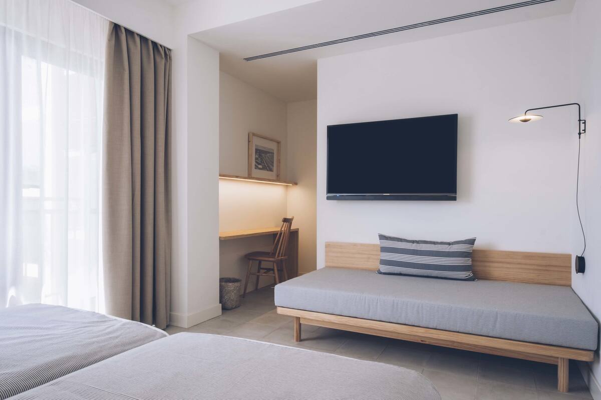 Ein Hotelzimmer mit Bett, Schreibtisch, Stuhl und einem an der Wand befestigten Fernseher.