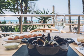 Una mesa de comedor con un plato de mariscos, una copa de vino blanco y un bol de salsa.