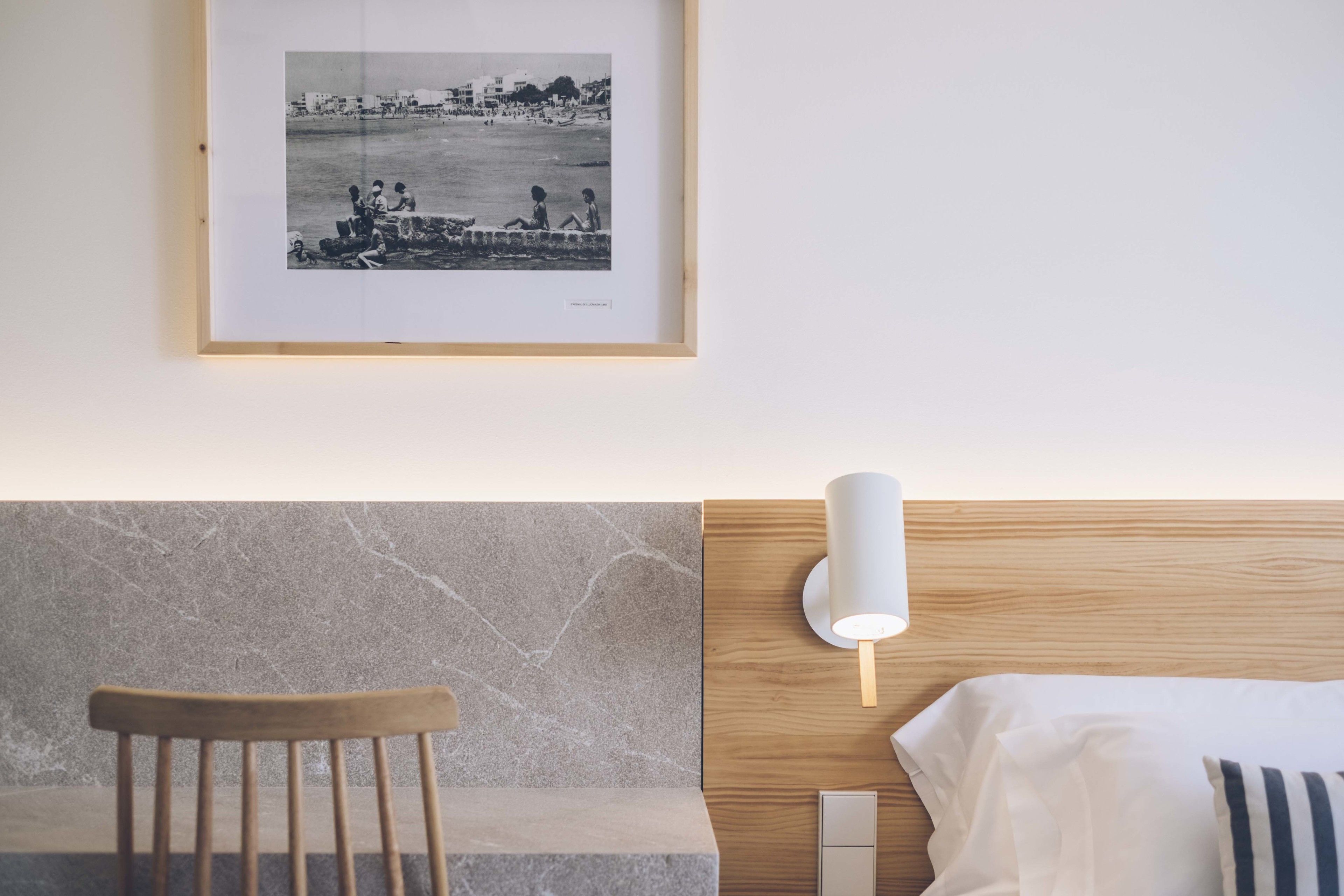 Habitación de hotel con una cama, una silla, una lámpara fijada a la pared y una fotografía enmarco.