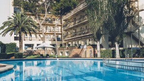 Una piscina con superficie de agua azul cristalina, rodeada por un edificio de varios pisos con balcones y una palmera.