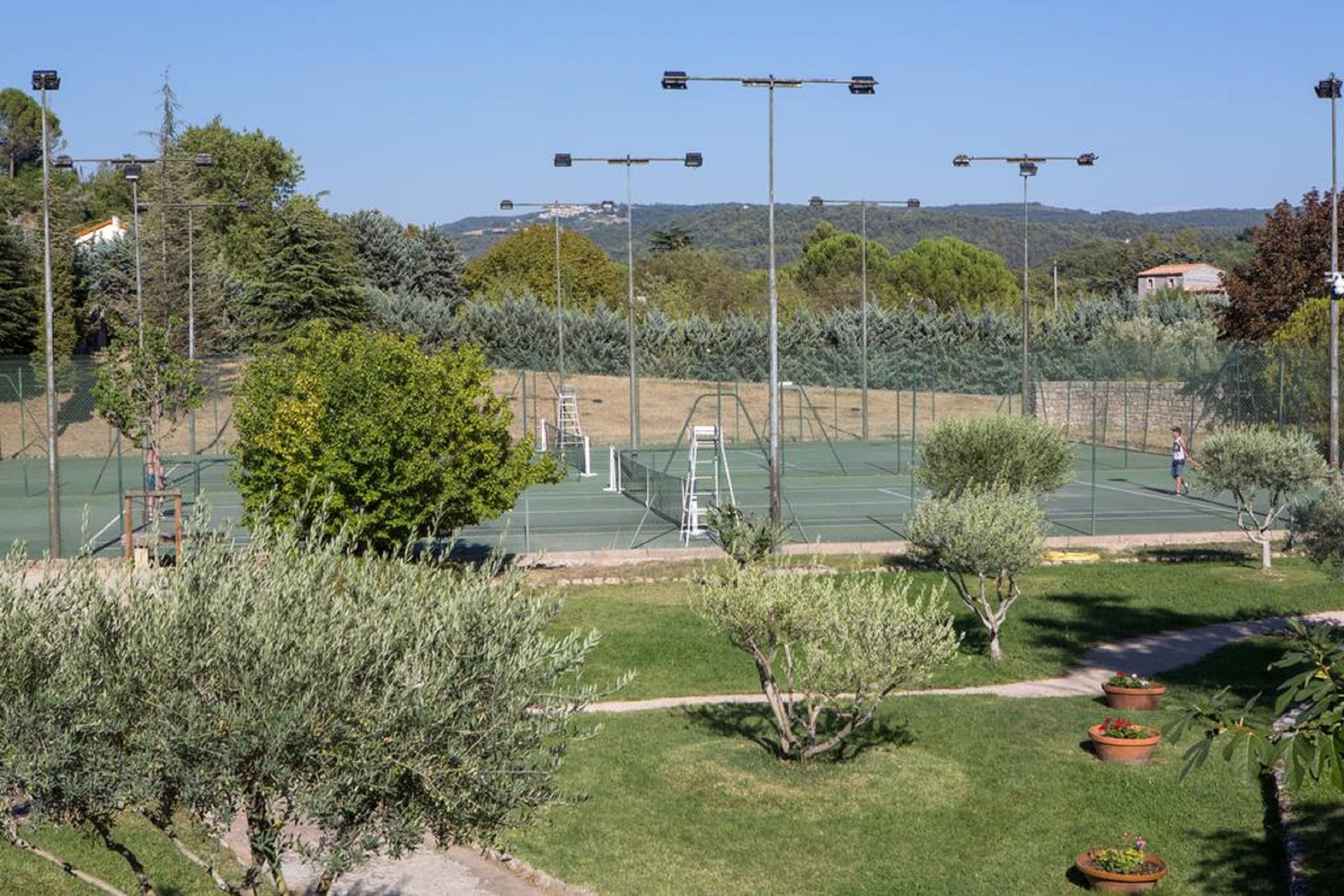 Una cancha de tenis al aire libre rodeada de vegetación y un cielo despejado.
