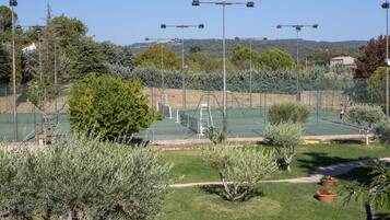 Una cancha de tenis al aire libre rodeada de vegetación y un cielo despejado.