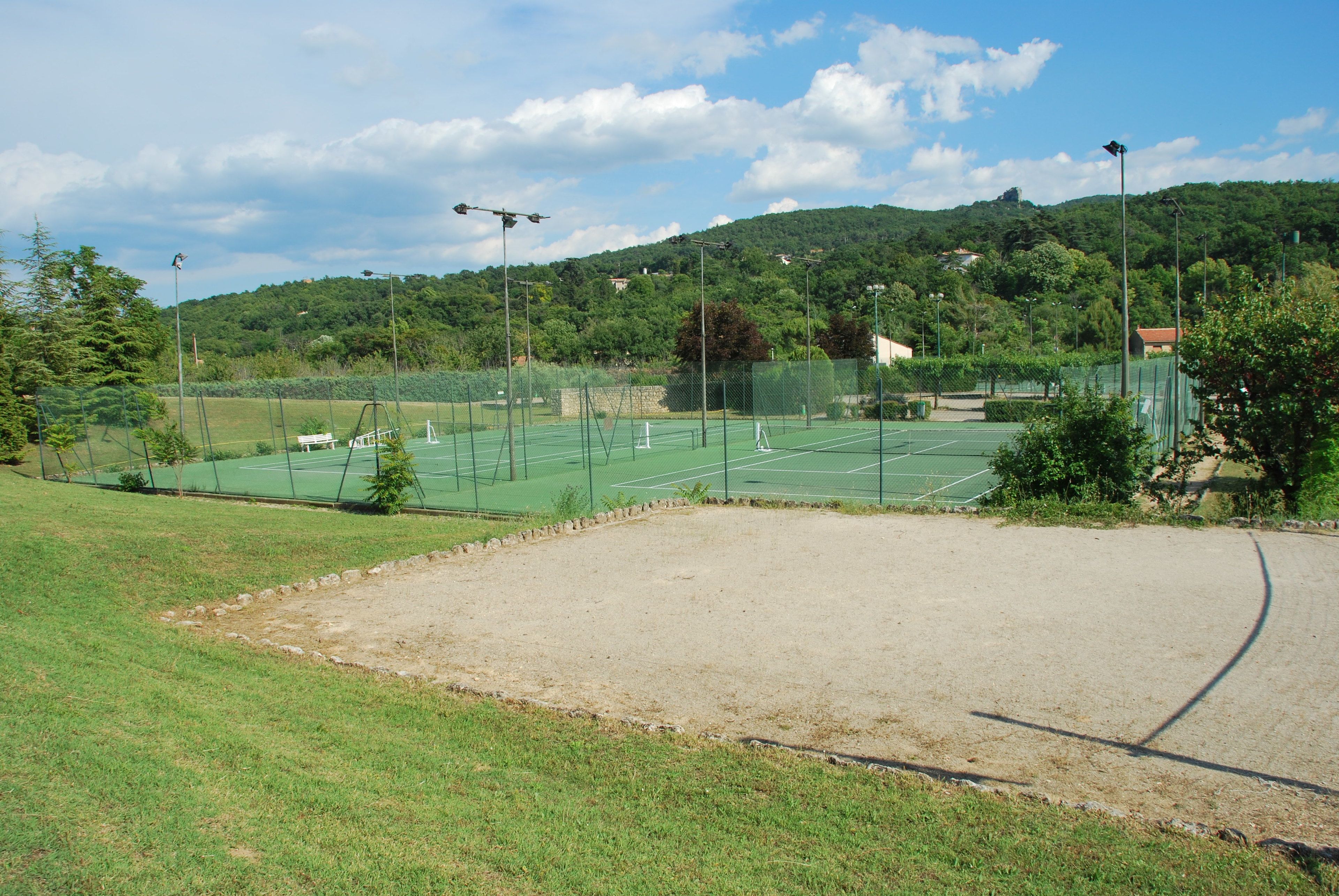 Een tennisbaan met een net, omringd door een groene hekken en een zandgebied op de voorgrond.