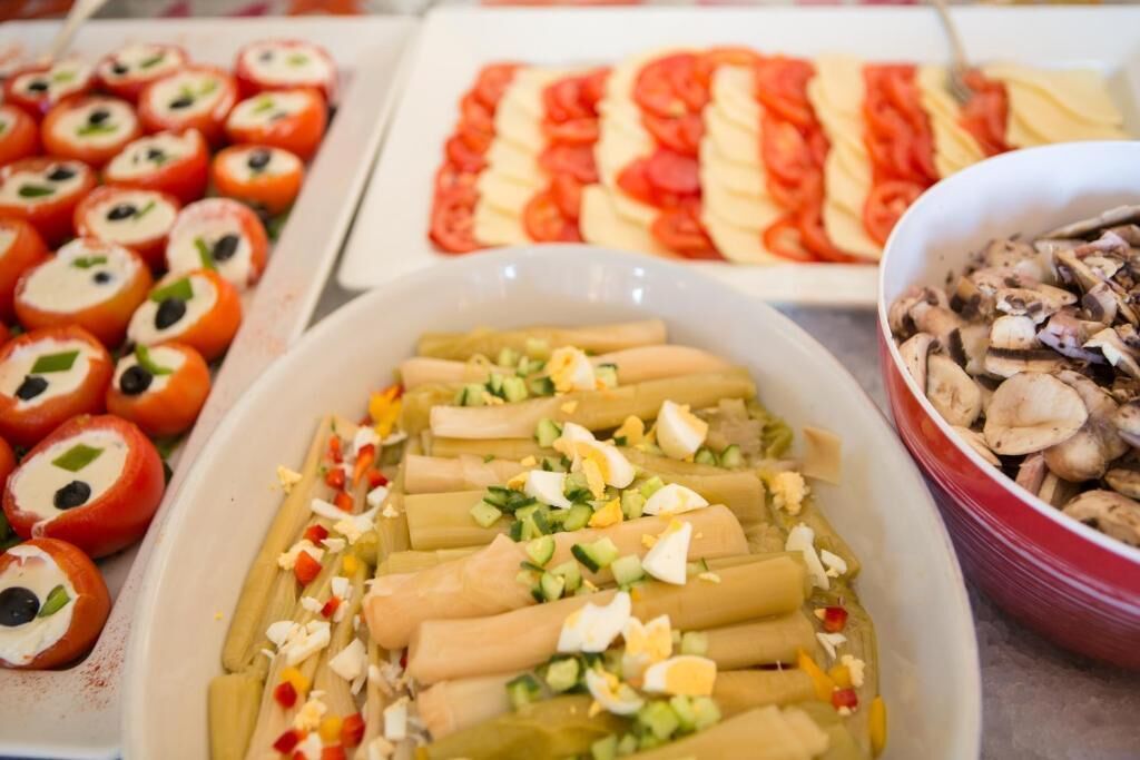 Een buffet met diverse gerechtjes, waaronder rolletjes groenten, plakjes tomaat en een schaal met champignons.