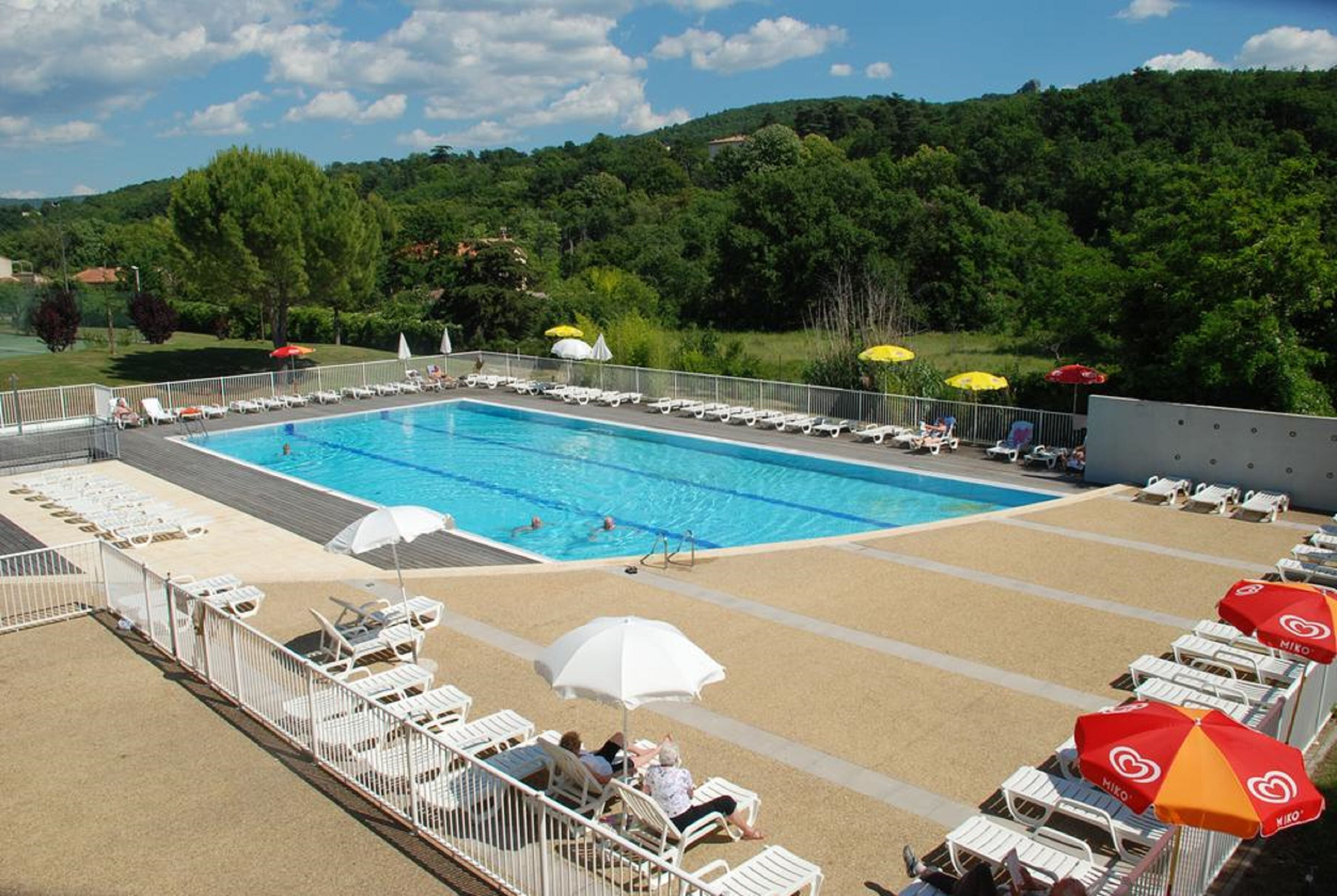 A swimming pool with lounge chairs and umbrellas, surrounded by a fence.