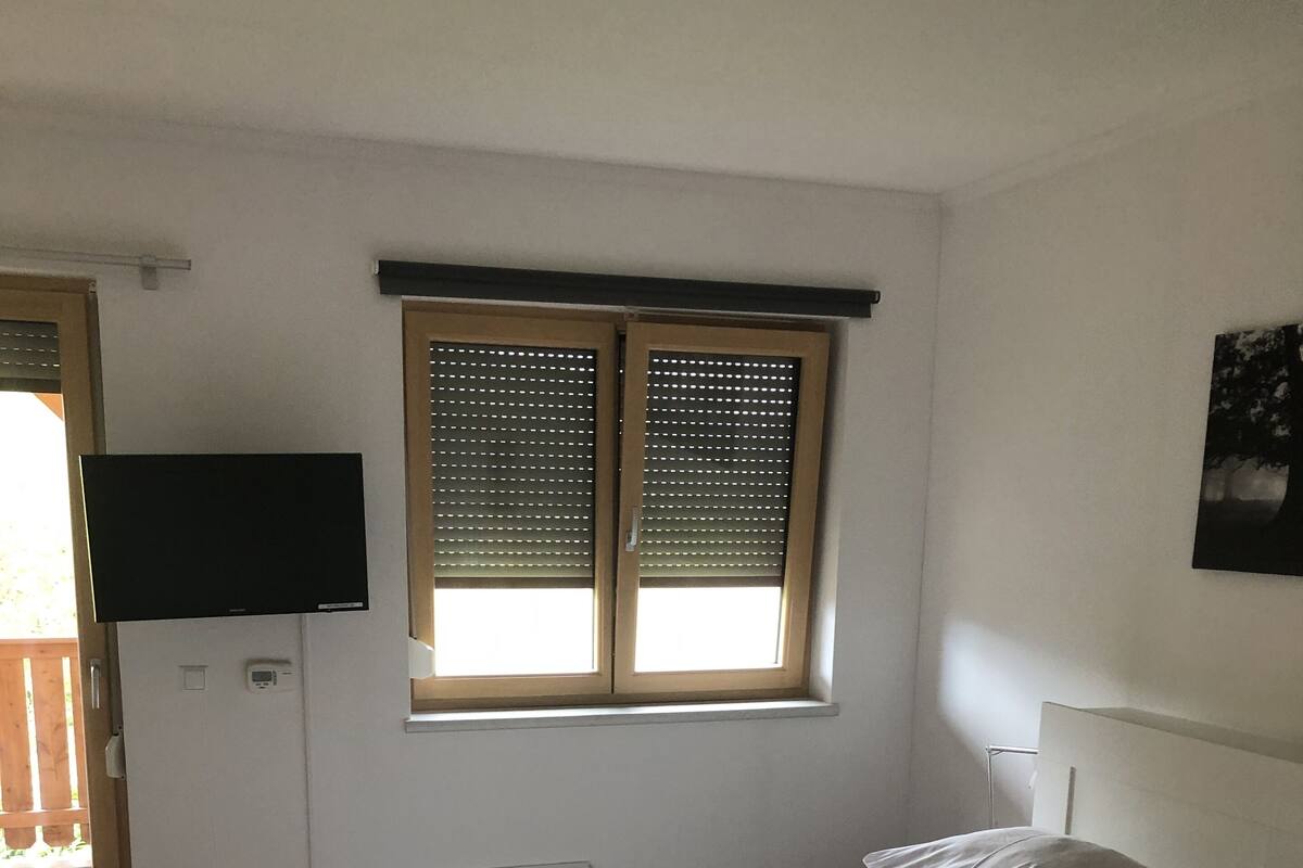 Una camera da letto con un letto, una finestra con persiane, una TV a muro e un'uscita verso un'area esterna.