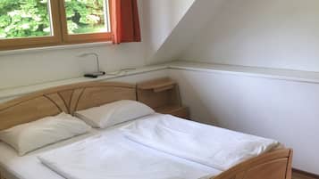 Ein Schlafzimmer mit einem hölzernen Bett, einem Nachttisch, einem Fenster mit Vorhängen und Blick ins Grüne.