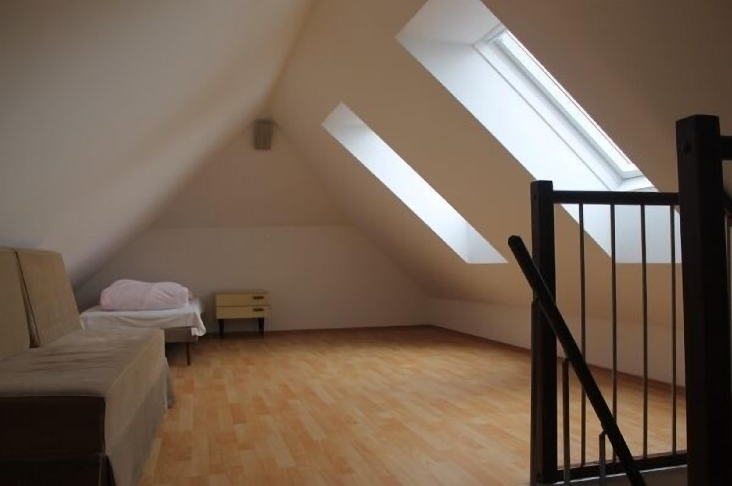 Ein kleiner Raum mit geneigtem Dach, einem Bett, einem Nachttisch und einem Fenster.