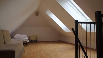 Ein kleiner Raum mit geneigtem Dach, einem Bett, einem Nachttisch und einem Fenster.