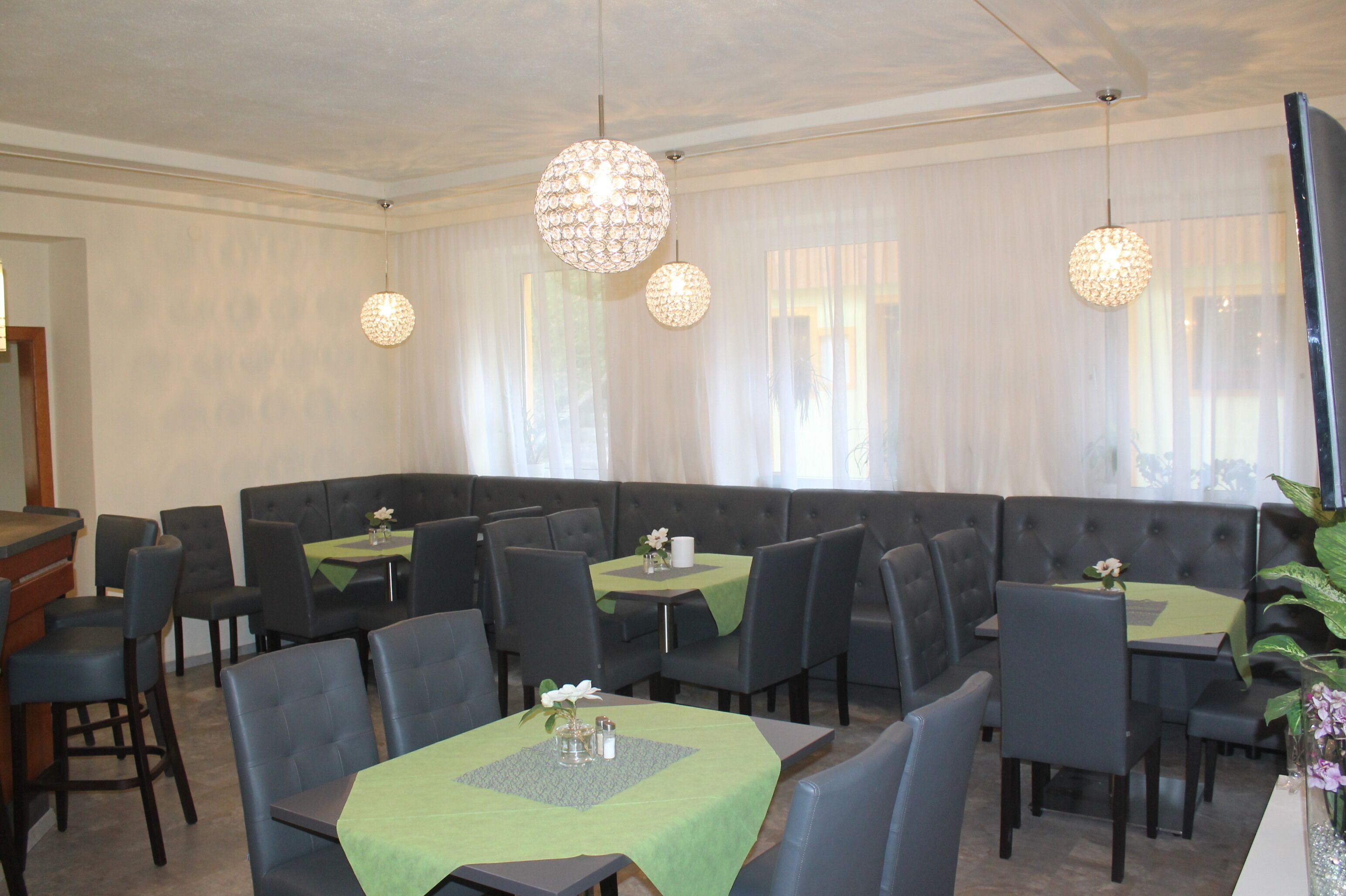 A restaurant with a green tablecloth, black chairs, and a large cushioned seating area.