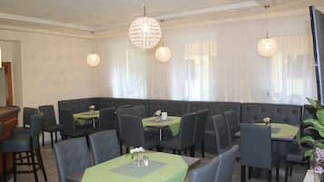 A restaurant with a green tablecloth, black chairs, and a large cushioned seating area.