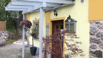 Un edifici amb façana groga, fonaments de pedra i una zona de terrassa coberta amb plantes en testos.