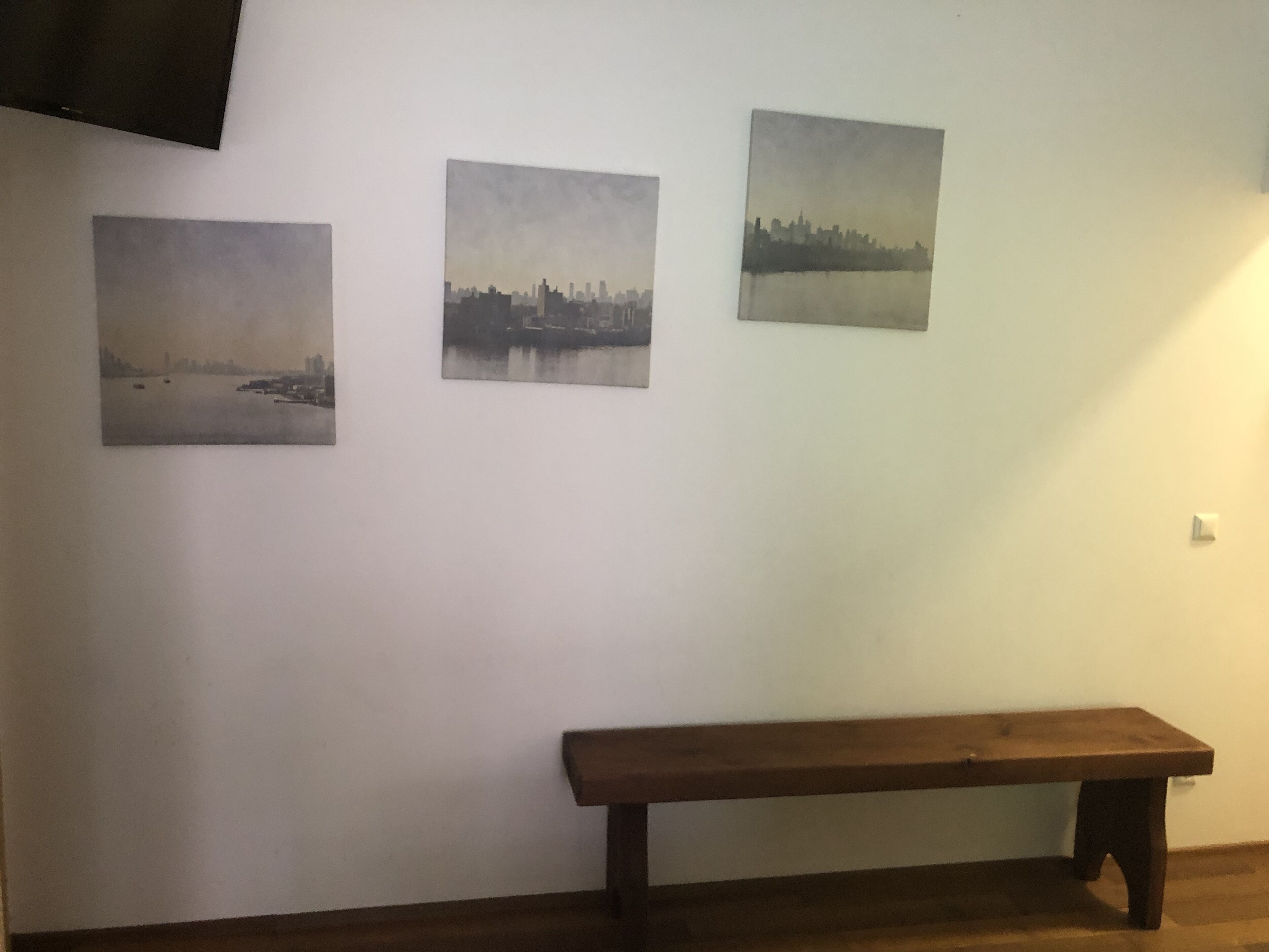 Una habitación con tres cuadros de paisajes urbanos en la pared y un banco de madera al frente.