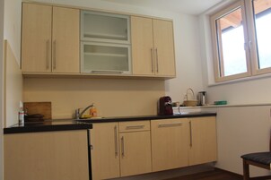 A compact kitchen with light wooden cabinets, a black countertop, and a window above the sink.