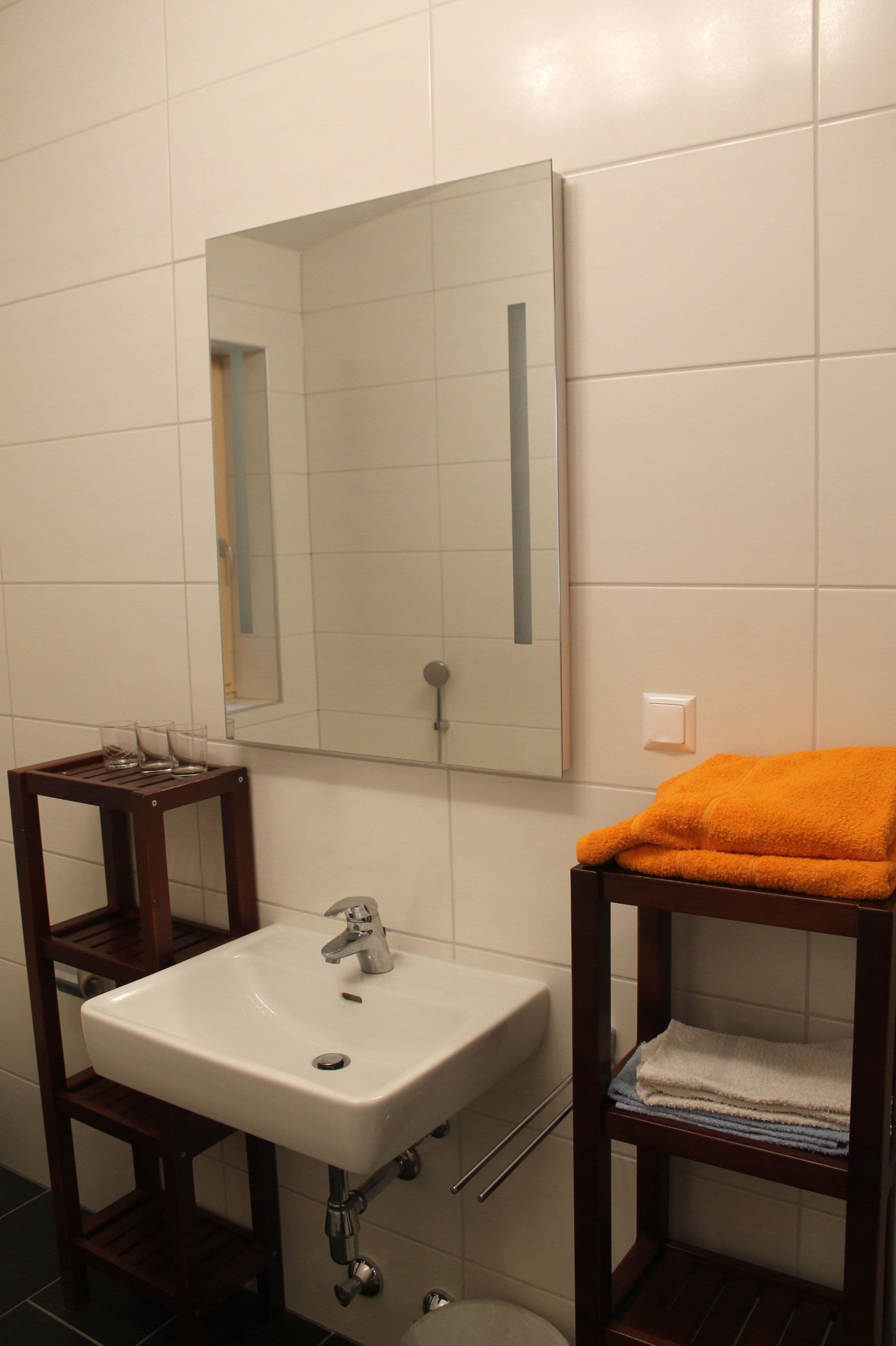 A bathroom with a white sink, a mirror, and a wooden shelf with a towel.