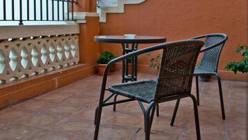 Una terraza con una mesa, dos sillas, una planta en maceta y una baranda decorativa.