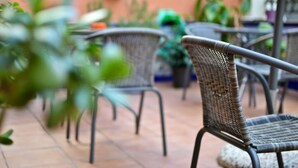 Des chaises et des tables en osier disposées à l’extérieur sur une terrasse carrelée.