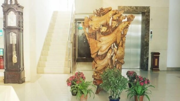 Un hall d’entrée avec un escalier, une grande sculpture en bois et des plantes en pot.