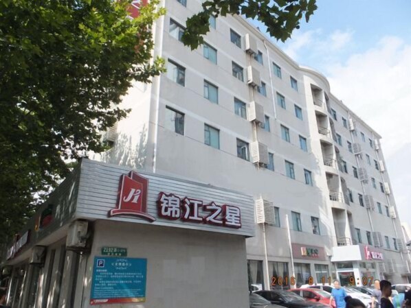 A hotel with a sign in Chinese characters, a parking sign, and a multi-story building in the background.