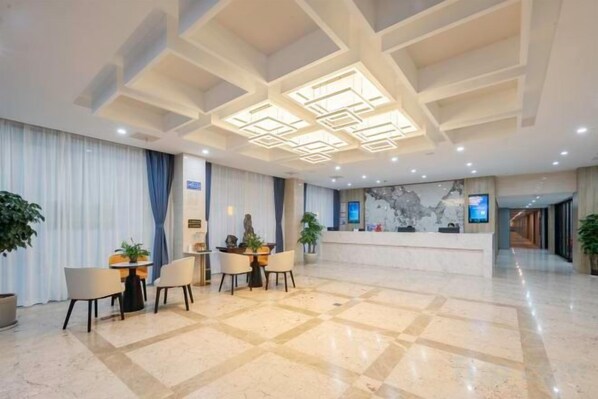 Un vestíbulo de hotel con mostrador de recepción, zona de estar y suelo de mármol.