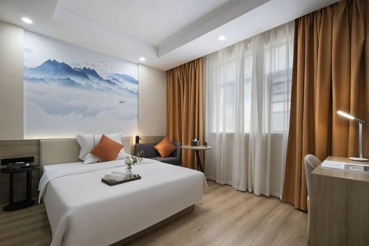 A hotel room with a large bed, a desk, a chair, a nightstand, and a wall-mounted TV.