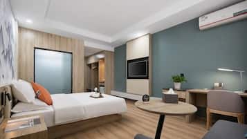 A modern hotel room with a bed, a desk, a chair, a TV, and a small table.