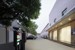 A street view with a parking meter, parked cars, and a building with large windows. - Kaiyue Business Hotel（Ninefang City Shop,Northmen Road ） (KUNSHAN)