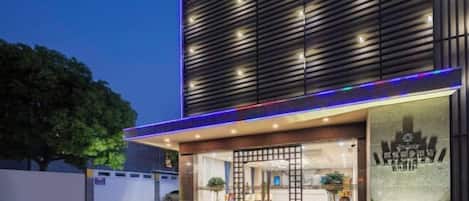 A modern hotel entrance with a glass facade, a wooden slatted wall, and a well-lit reception area.