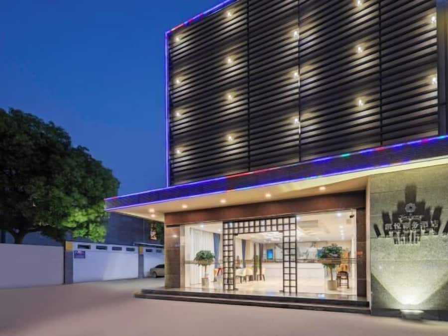 A modern hotel entrance with a glass facade, a wooden slatted wall, and a well-lit reception area.