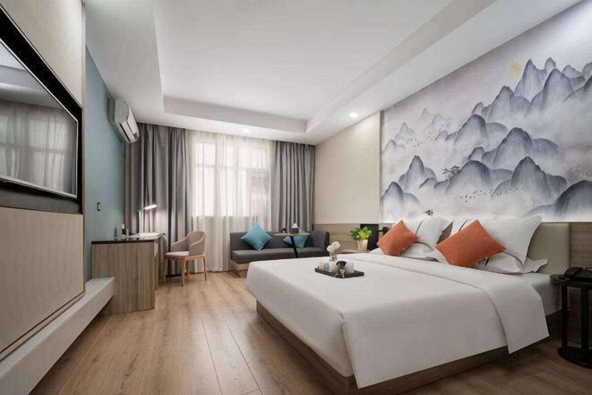 Habitación de hotel con cama, escritorio, silla, televisor y un cuadro grande en la pared.