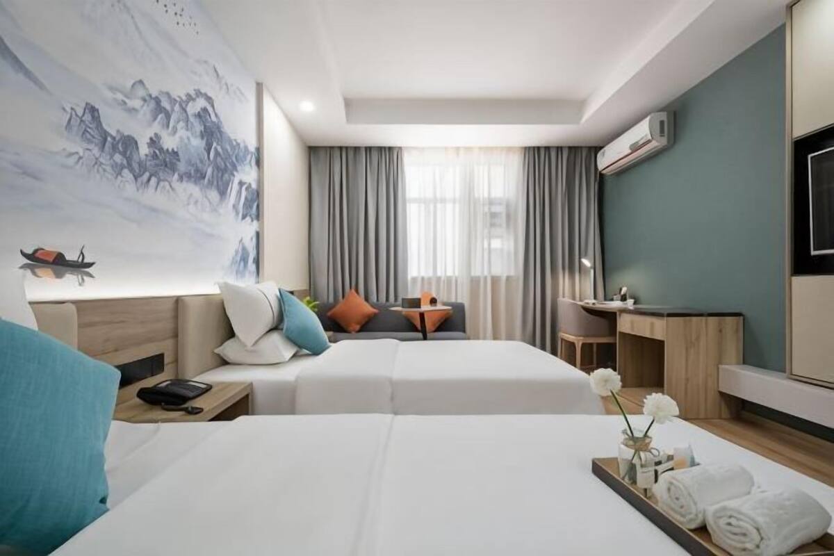 Habitación de hotel con dos camas, un escritorio, una silla, un televisor y un cuadro en la pared.