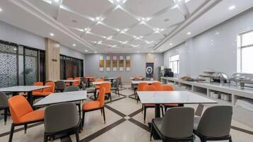 A dining area with tables and chairs, a buffet line, and a kitchen in the background.