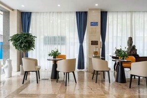 A hotel lobby with a reception desk, seating area, and a large plant. - Kaiyue Business Hotel（Ninefang City Shop,Northmen Road ） (KUNSHAN)