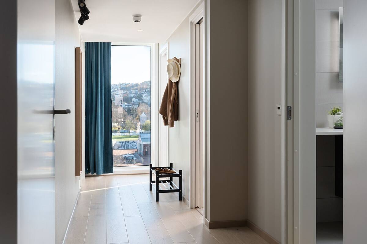A hallway with a view to the outside, a bench, and a door with a hat hanging on it.