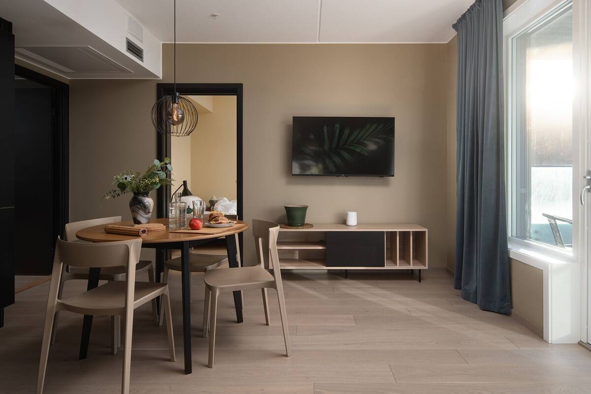 A modern dining area with a round table, chairs, and a TV mounted on the wall.